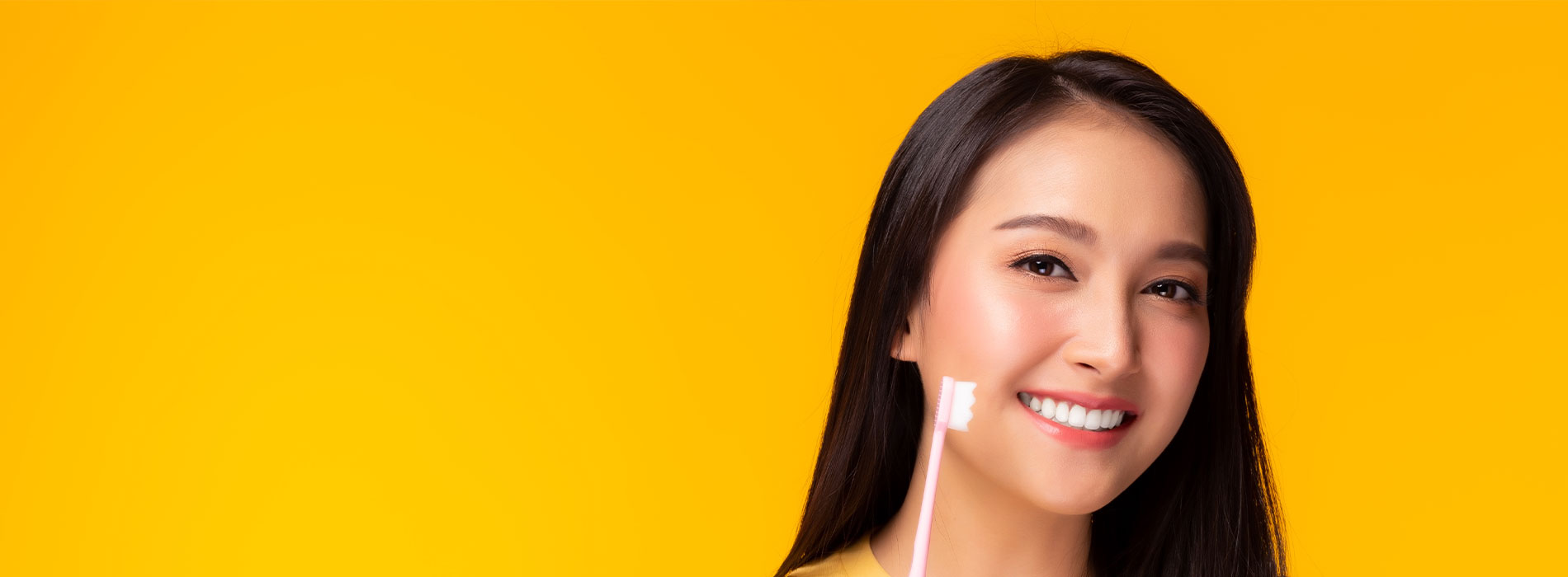 A woman with dark hair smiling at the camera against a yellow background with a blurred strip of black at the bottom.