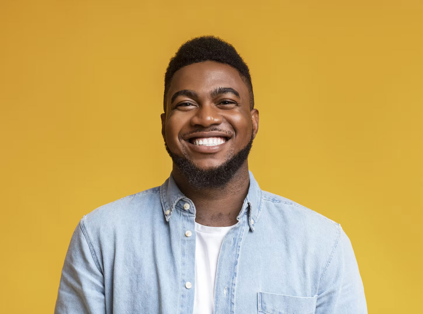 A man with a beard smiling at the camera against a yellow background.