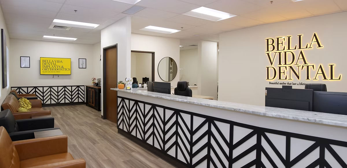 The image shows an interior view of a dental office reception area with a modern design featuring a sign that reads  Bella Vida Dental.