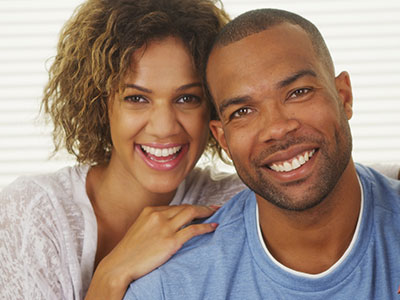 A man and woman posing closely together, smiling at the camera, with the man wearing a short beard and the woman with curly hair.