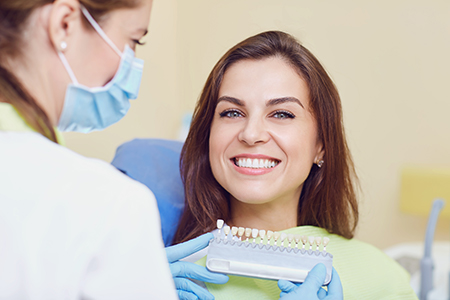 The image depicts a dental professional assisting a patient during a dental appointment, with both individuals smiling at the camera.