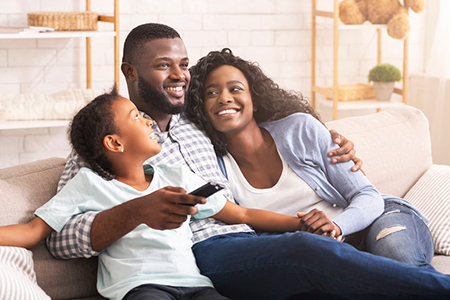 A family sitting together on a couch, with a man holding a child, smiling at the camera.
