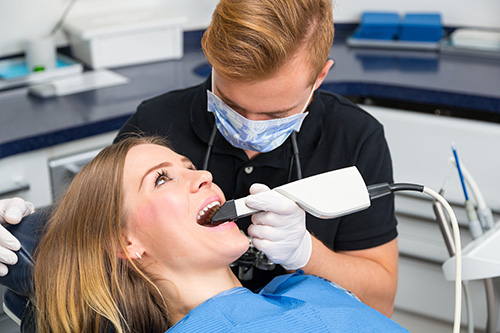 The image shows a dental professional performing a procedure on a patient in a dental office setting, with visible dental equipment and tools.