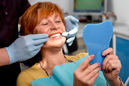Woman in dental chair with blue toothbrush, smiling at camera.