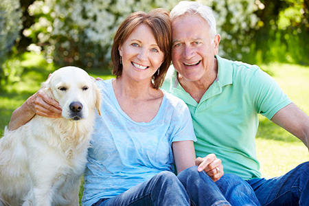A man and woman are sitting outdoors with a golden retriever dog between them, smiling at the camera.