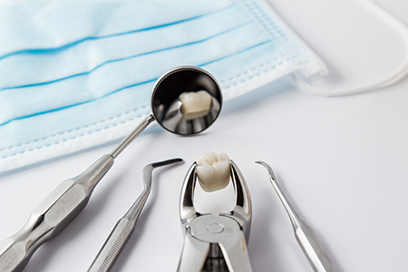 Image depicts a collection of dental tools including a toothbrush with a single tooth, a pair of scissors, and several other instruments arranged on a white surface with a blue cloth background.