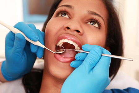 A woman sitting in a dental chair receiving oral care with a dental hygienist working on her teeth.
