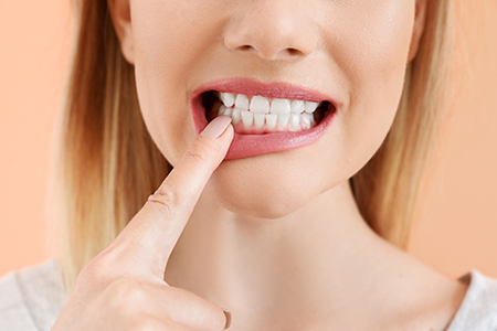 The image shows a woman with her finger on her teeth, possibly brushing or cleaning them, against a blurred background.