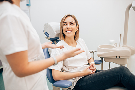 A woman sitting in a dental chair with a smile on her face, being attended by two dental professionals who are focused on her care.