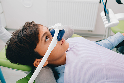 A young person seated in a dental chair with a dental device strapped over their eyes, appearing to be experiencing an immersive dental visit using virtual reality technology.