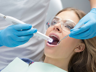 The image shows a person lying down with their mouth open while being attended to by dental professionals who are holding a device near their mouth, likely for dental treatment or examination.